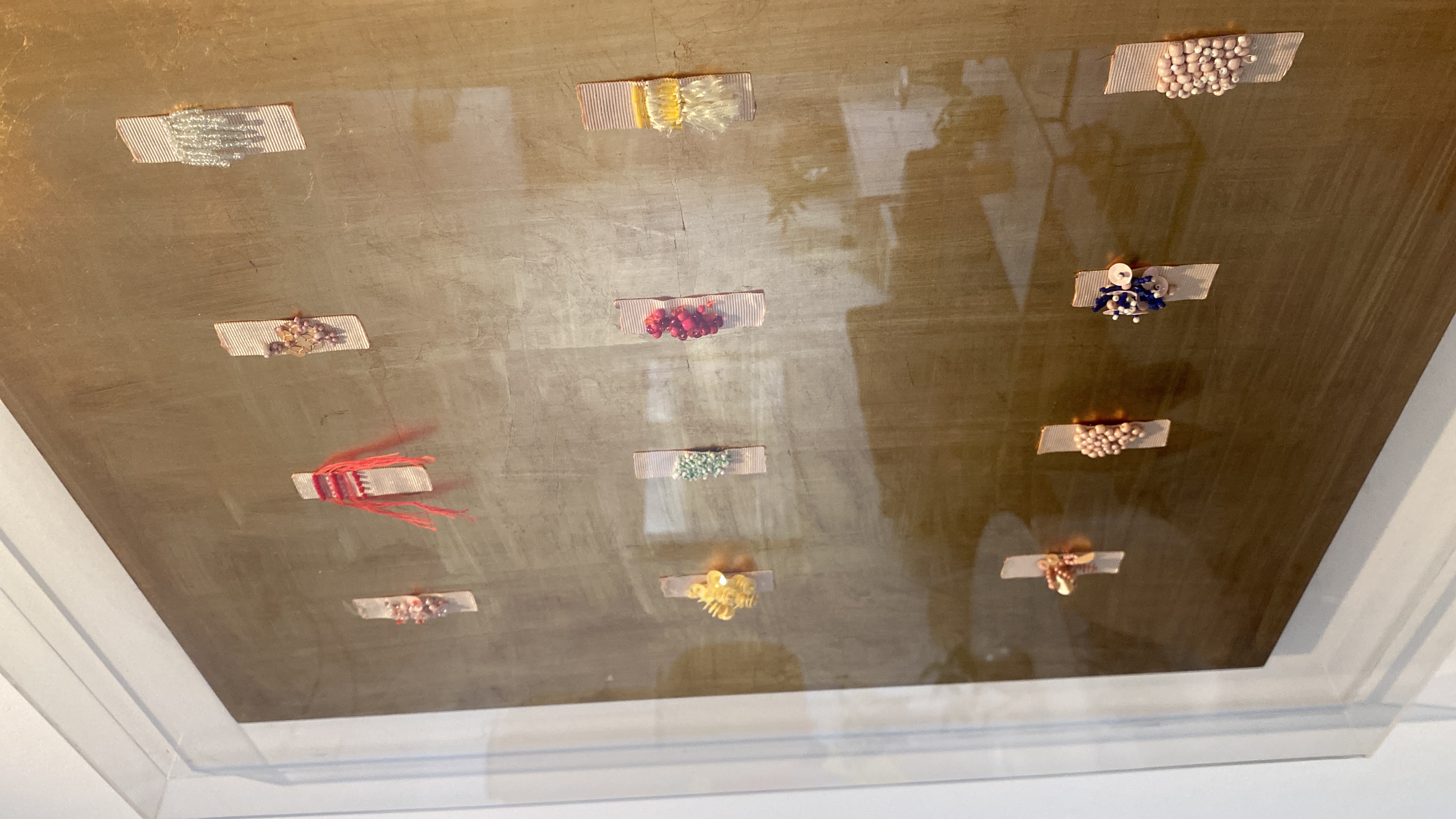 Twelve hand-embroidered miniatures arranged on a gold-leaf panel, showing the scale and detail of the work